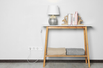 Lamp with books on wooden table near white wall, space for text