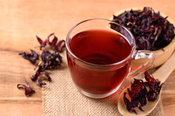 Wall Mural - Roselle tea in cup glass with dry roselle on wooden background, Herbal drink for reduction in blood pressure