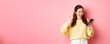© Mix and Match Studio - Happy pretty woman saying yes, holding mobile phone and making thumbs up gesture, approve good thing, standing against pink background