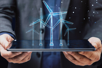 Poster - Close up of businessman hand holding tablet with glowing digital wind mill turbine hologram on blue background. Wind generator concept.