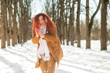 Fat caucasian woman playing snowballs in the park. 