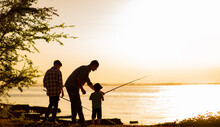 Family Dad And Two Sons Are Fishing At Sunset, Silhouette Of A Man And Two Boys.
