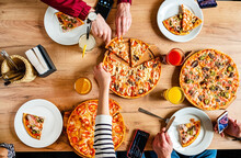 Hands Taking Pizza Slices From Wooden Table