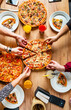 © Maksim Shebeko - Hands taking pizza slices from wooden table