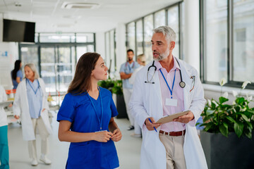 Portrait of elderly doctor with his younger colleague at hospital corridor. Health care concept.