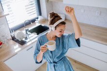Young Woman Listening Music And Enjoying Cup Of Coffee At Morning, In Her Kitchen.