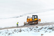 Industrial worker in front of heavy duty bulldozer on road building construction site in winter