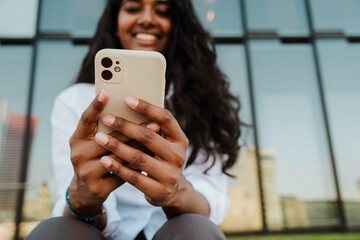 Wall Mural - Young indian woman using cellphone while sitting by building outdoors