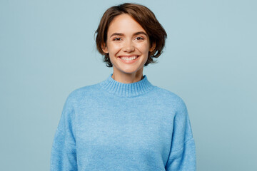 Wall Mural - Young cheerful joyful satisfied smiling happy friendly caucasian woman in knitted sweater looking camera isolated on plain pastel light blue cyan background studio portrait. People lifestyle concept