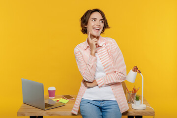 Wall Mural - Young successful fun employee business woman wear casual shirt work stand near office desk with pc laptop prop up chin look aside isolated on plain yellow color background Achievement career concept.