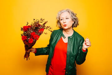 Portrait of a senior woman dancing with a red roses bouquet over a yellow background