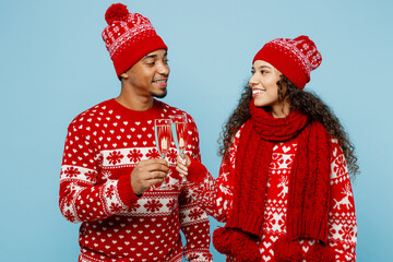 Wall Mural - Merry young fun couple two man woman wear red Christmas sweater Santa hat posing drink champagne clink raise toast isolated on plain pastel light blue background. Happy New Year 2023 holiday concept.