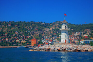 Wall Mural - Landscape of lighthouse in the port of Alanya. White lighthouse in seaport of Alanya with concrete path and stones. Copy space for text.