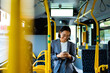 © Drobot Dean - Asian woman smiling and using smart phone while standing in a bus