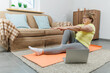 © SOLOTU - Mature woman exercising on the floor in front of laptop in the living room at home