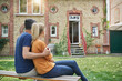 © Westend61 - Man embracing woman looking at house sitting on bench in garden