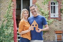 Happy couple holding wooden house model in garden