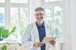 © Westend61 - Happy mature doctor standing with tablet PC in medical practice