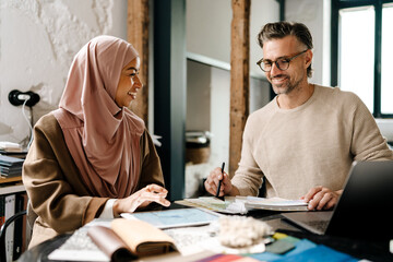 Two multinational colleagues working with laptop computer at workshop