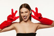 © master1305 - Portrait of beautiful young woman with straight brown hair and dark makeup posing in red rubber gloves over white background. Party look