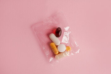 Assorted pharmaceutical medicine pills, tablets and capsules in small sachet on pink background