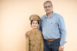 © GAJENDRRA BHATI  - Happy indian kid wearing police uniform dress standing with his proud grandfather isolated over beige studio background.