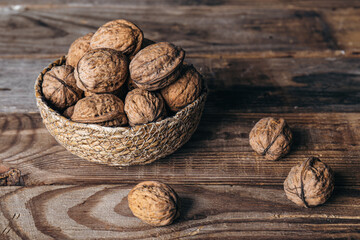 Wall Mural - Close-up, whole walnuts in a wicker bowl on a wooden background.