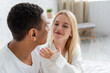 © LIGHTFIELD STUDIOS - happy young woman holding hand near blurred african american man in bedroom