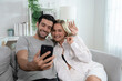 © Basicdog - Caucasian couple sitting on the couch and looking at the smartphone screen.