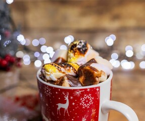 Sticker - Tasty hot chocolate with marshmallows in a red Christmas cup against the blurry background of lights