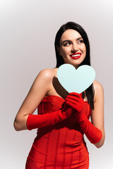 Canvas Print - Positive and stylish woman in red gloves and dress holding paper heart isolated on grey