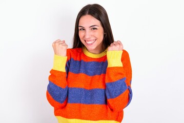 Young caucasian woman wearing colorful knitted sweater over white background celebrating surprised and amazed for success with arms raised and open eyes. Winner concept.