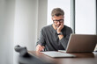 © gzorgz - Mddle aged businessman looking thoughtfully while using laptop and working at the office