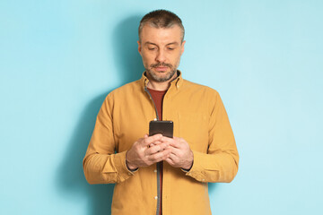 Poster - Mature caucasian man using cellphone, texting via smartphone, communicating online standing over blue background