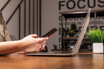 Poster - Hand holding smartphone, sitting at wooden office desk with laptop computer, PC. Working with information technologies, devices