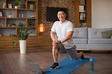 Excited mature korean man doing lunges, exercising for legs in living room interior, looking at camera and smiling