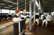 © pressmaster - Two young farmers in workwear standing by cowshed at working meeting and discussing opportunities of improvement of cattle keeping