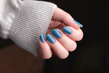 Wall Mural - Female hand in gray knitted sweater with beautiful manicure - blue glitter nails. Nail care concept