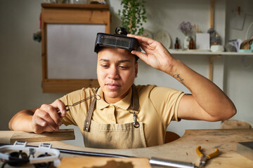 Wall Mural - Front view of female jeweler creating handmade art pieces at wooden table in rustic studio