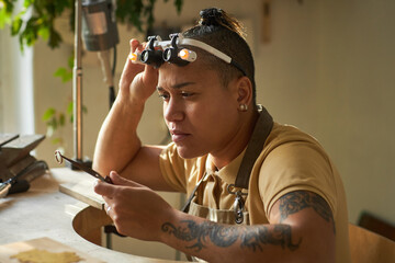 Wall Mural - Side view portrait of black female jeweler creating handmade gold ring and wearing magnifying goggles