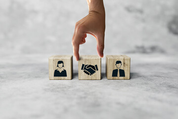 The hand holds wooden wooden blocks with icons of a woman and a man and shaking hands in the act of consent. The concept of divorce, agreement, mediation, the role of the mediator.