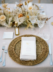 Wall Mural - Above view of a handmade straw plate with napkin near cutlery and floral arrangements on festive banquet