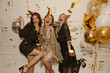 Crazy young interracial women in elegant outfit celebrating birthday amid balloons and confetti. Girlfriends closing their eyes have fun, dance, drink alcoholic cocktails. Party concept