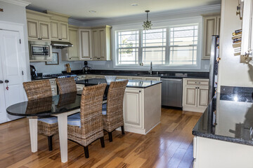 A cream colored new construction kitchen with black granite countertops and wood flooring and stainless steel appliances