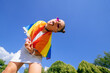 A young woman develops a rainbow flag against the sky