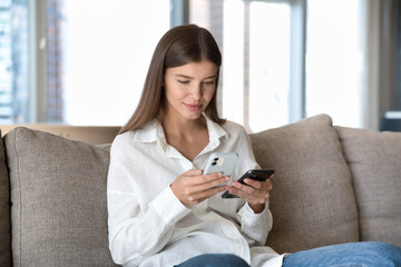 Engaged young adult digital addict girl using two smartphones for data, file transfer, prompting wireless connection technology, domestic internet communication, online service, app