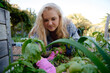 © StratfordProductions - Happy young caucasian woman in checked shirt and gardening gloves by plants in garden center