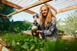 © StratfordProductions - Happy young caucasian woman in checked shirt watering plants in plant nursery