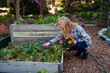 © StratfordProductions - Profile view of young caucasian woman in checked shirt crouching with flowers in plant nursery