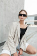 © alones - Fashionable urban pretty woman hipster model with black cool sunglasses in trendy fashion casual clothes with blazer and top posing in the city